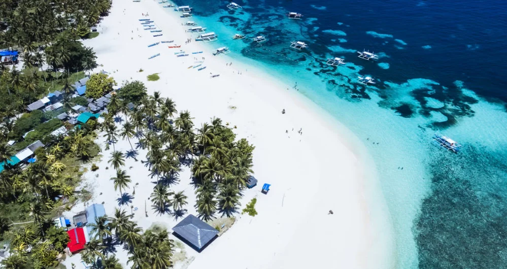 Aerial view of a white sand beach on Siargao, lined with coconut palms and outrigger boats moored on the reef
